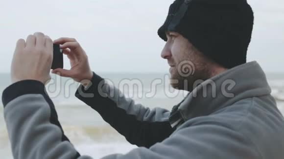 年轻的高加索人在风暴中的海上智能手机上拍照视频的预览图