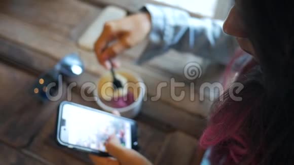 年轻的白种人女孩有着彩色粉红头发使用手机和吃冰淇淋在咖啡馆高清慢速运动戈芬加视频的预览图