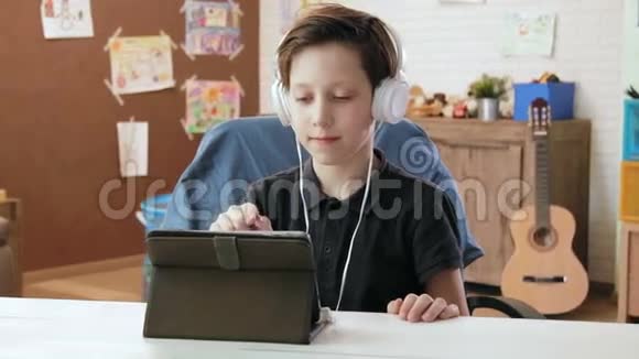 可爱的小男孩戴着耳机在他的数码平板电脑上听音乐视频的预览图