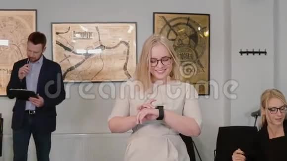 年轻的金发女人穿过现代办公室看着智能手表女孩使用新技术慢动作视频的预览图