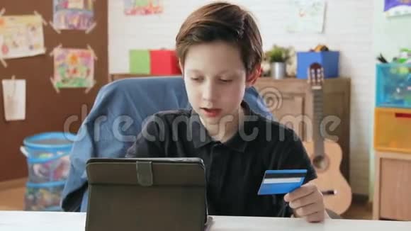 可爱的小男孩在网上购物使用输入信用卡号码使用数字平板电脑并高兴后制作视频的预览图