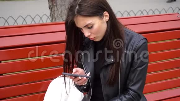 女孩在公园的长凳上用手机视频的预览图