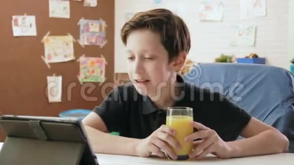 可爱的小男孩喝着橙汁看着滑稽的视频视频的预览图
