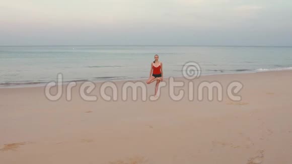 日出前在海滩上穿红色运动服的女人练习瑜伽健身运动视频的预览图