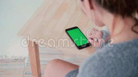 女人坐在餐桌前在厨房喝咖啡的后景布鲁内特女孩使用智能手机绿色屏幕视频的预览图