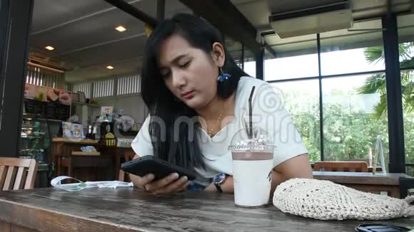 泰国女人坐在咖啡厅放松玩智能手机喝巧克力视频的预览图