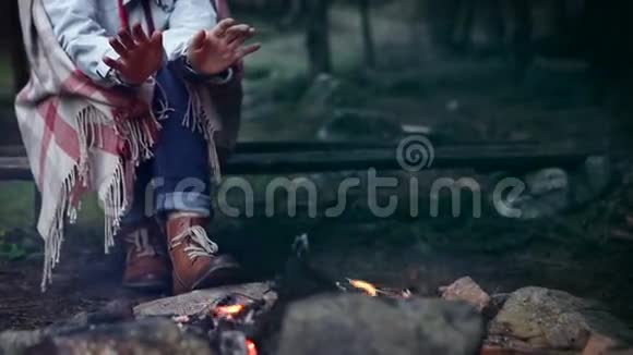裹着格子花格子的女人在篝火上温暖着她冰冷的双手视频的预览图