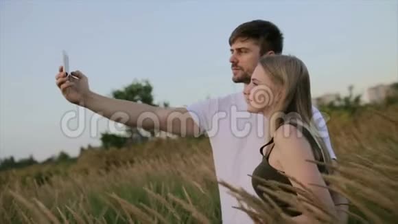一对相爱的夫妻和一个漂亮的年轻女人在一起在日落或日出时在田野上自拍视频的预览图