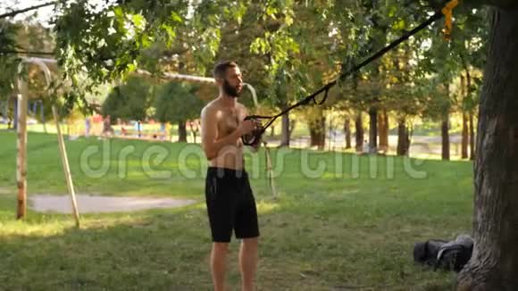 有胡子的年轻人开始在公园里用健身环锻炼4K慢节奏的电影视频的预览图