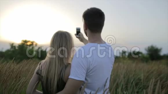 一对相爱的夫妻和一个漂亮的年轻女人在一起在日落或日出时在田野上自拍视频的预览图