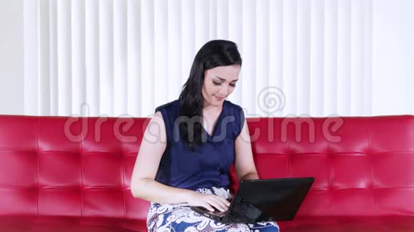休闲女性在红色沙发上使用笔记本电脑视频的预览图