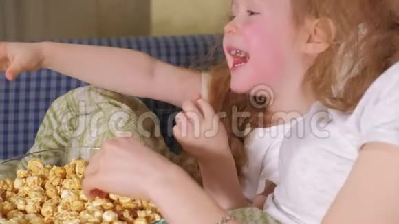 充满爱意的家庭妈妈和她女儿的小女孩正在房间的床上吃爆米花电视前面视频的预览图