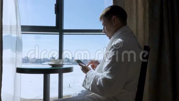 一个年轻有魅力的男人一个商人坐在窗边的桌子旁喝茶喝咖啡写短信视频的预览图
