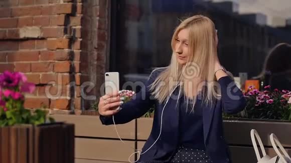 穿着西装的年轻女商人在智能手机上听音乐自拍美丽的金发女郎正躺在视频的预览图