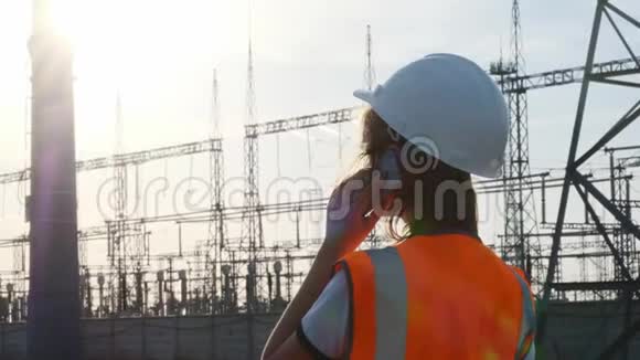 一位戴着白色头盔穿着橙色防护背心的女工程师在检查一个有电线和电力的发电站视频的预览图