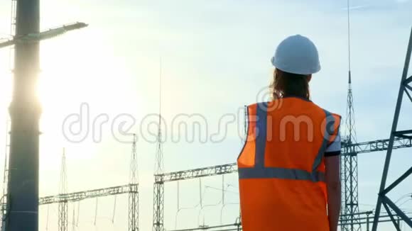 一位戴着白色头盔穿着橙色防护背心的女工程师在检查一个有电线和电力的发电站视频的预览图