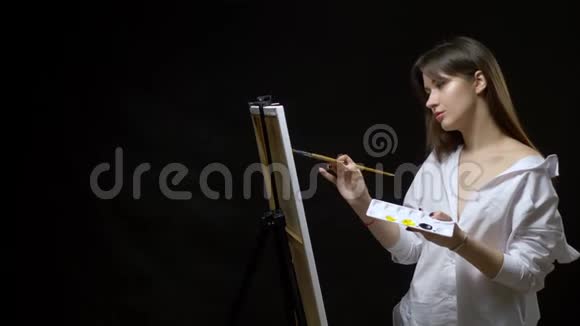可爱的女孩艺术家用油画颜料在画布上画一幅画黑色背景视频的预览图