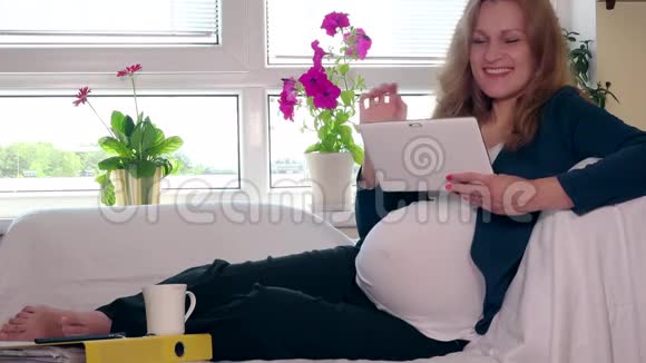 玩的孕妇在家喝咖啡在沙发上用平板电脑视频的预览图