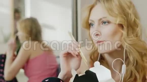 年轻有魅力的女人在耳机上听音乐在纸盒里用筷子吃米饭视频的预览图
