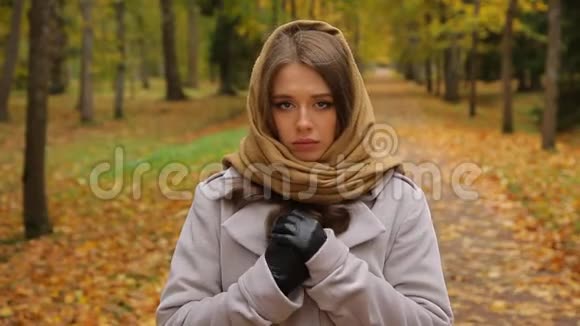 秋天公园里穿着灰色外套和针织围巾的美丽悲伤的白种人女人视频的预览图