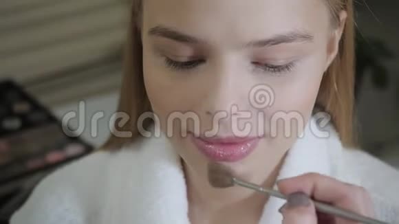 粉底刷化妆师为金发模特创造美丽的妆容美容和水疗中心概念视频的预览图