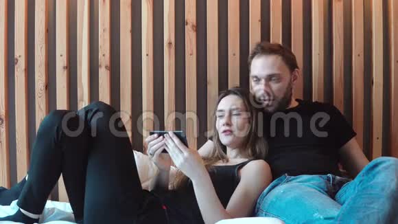 幸福夫妇用智能手机看照片躺在床上年轻的男人和女人说话花时间在一起视频的预览图