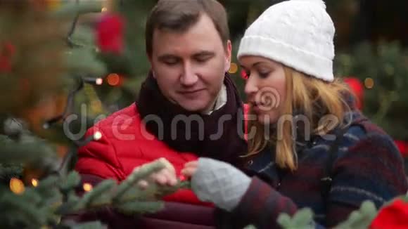 快乐夫妻在圣诞集市上选择圣诞树年轻的家庭在圣诞集市上聊天和接吻祝你快乐视频的预览图