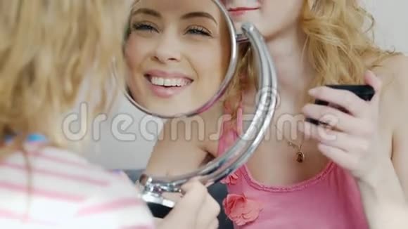 两个年轻的女朋友在家做化妆笑他的脸映在镜子里卧室里的睡衣派对视频的预览图