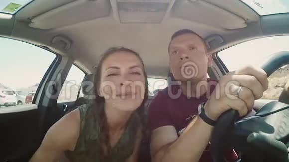 一对年轻夫妇在车里穿过岩石男人和女人玩得开心一起在路上做滑稽的脸视频的预览图