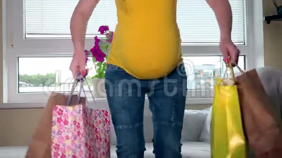 疲惫的孕妇带着五颜六色的袋子坐在沙发上购物后回家视频的预览图