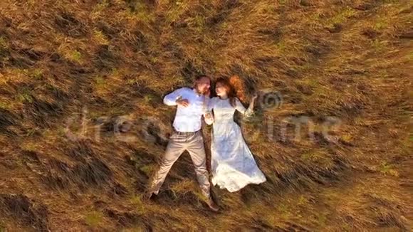 幸福的新婚夫妇躺在一片黄色的草地上空中飞行从上面看背景草地上美丽的年轻夫妇视频的预览图