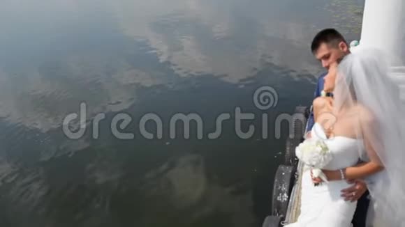 美丽的新娘和新郎站在湖边的背景上新婚夫妇幸福地站在码头上视频的预览图