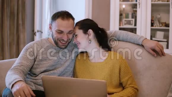 年轻夫妇坐在客厅的沙发上笑着用笔记本电脑上网视频的预览图