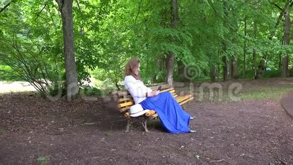 怀孕女性坐在公园长椅上浏览智能手机视频的预览图