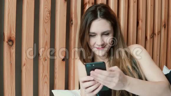 漂亮的年轻女人坐在沙发上用智能手机发短信客厅里微笑的女人视频的预览图