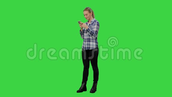 年轻漂亮的金发女人在智能手机上打字在绿色屏幕上微笑Chroma键视频的预览图