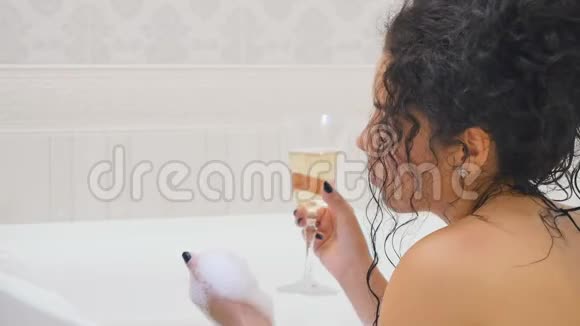 美丽的卷发带香槟的沐浴在泡沫中视频的预览图