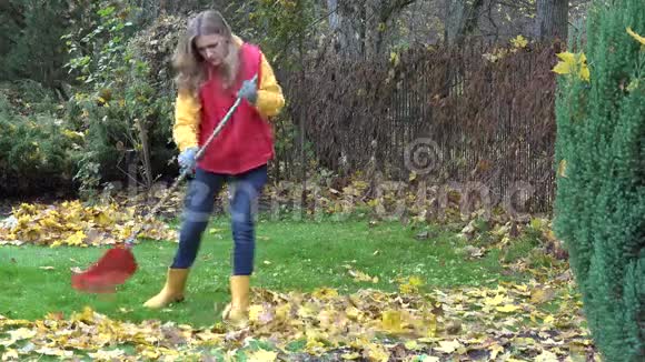 女人穿着背心牛仔裤和胶靴耙生动的黄色秋叶4K视频的预览图