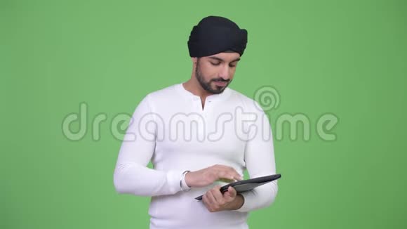 年轻的留着胡子的印度男人用数字平板电脑思考视频的预览图