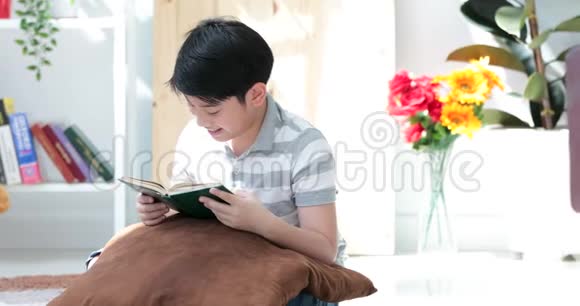 亚洲可爱的男孩在家地板上读一本书面带笑容视频的预览图