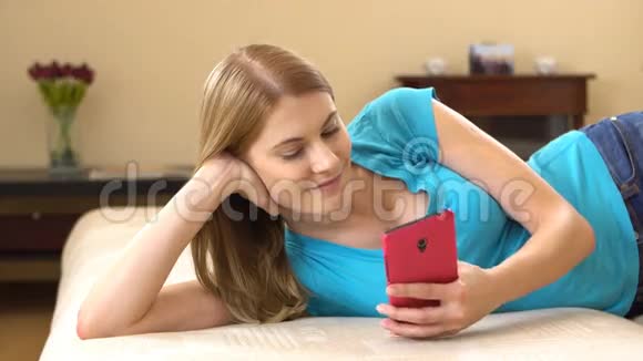 美丽迷人的年轻女子穿着蓝色t恤躺在沙发上在电话里交谈视频的预览图