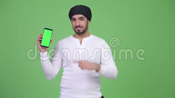 年轻快乐的留着胡子的印度男人带着电话竖起大拇指视频的预览图