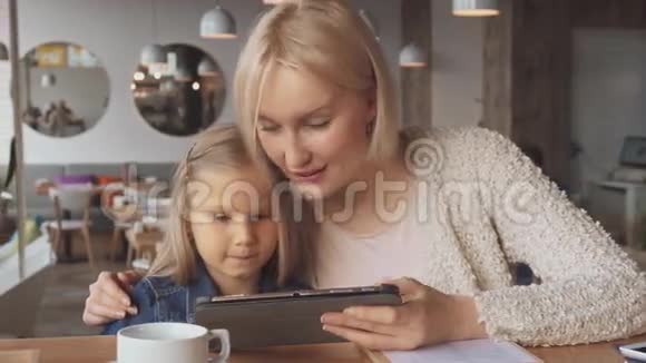 母亲和女儿在咖啡馆里用平板电脑视频的预览图