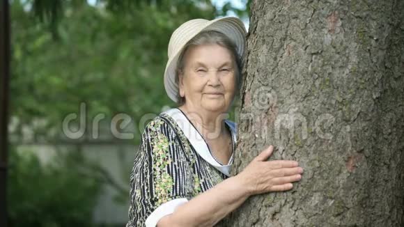 一位抱着树微笑的老妇人在镜头前视频的预览图