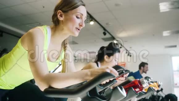 一位美丽的女士在健身房骑自行车时微笑的侧景视频的预览图