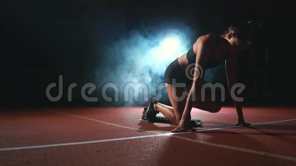 黑暗背景下的女运动员正准备从跑步机上的垫子上进行越野冲刺视频的预览图