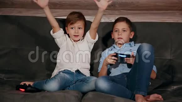 两个兄弟坐在沙发上非常情绪化地用无线操纵杆玩电子游戏视频的预览图