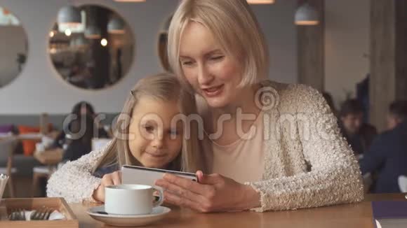 母亲和女儿在咖啡馆里使用智能手机视频的预览图