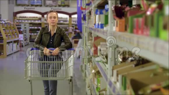 女孩走在批发货架上在商店的手推车里取货漂亮的年轻妻子在超市购物视频的预览图