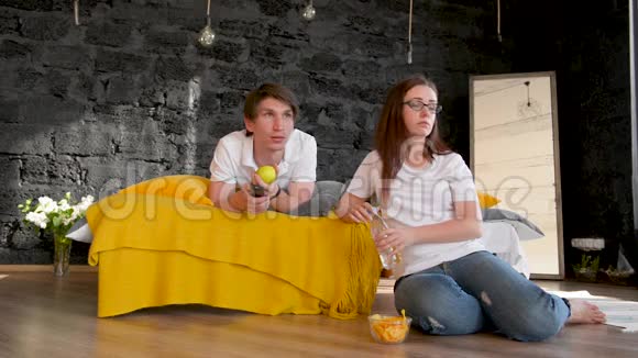 一对年轻夫妇一个男人和一个女孩躺在家里的床上看电视发誓不能决定他们会看什么视频的预览图